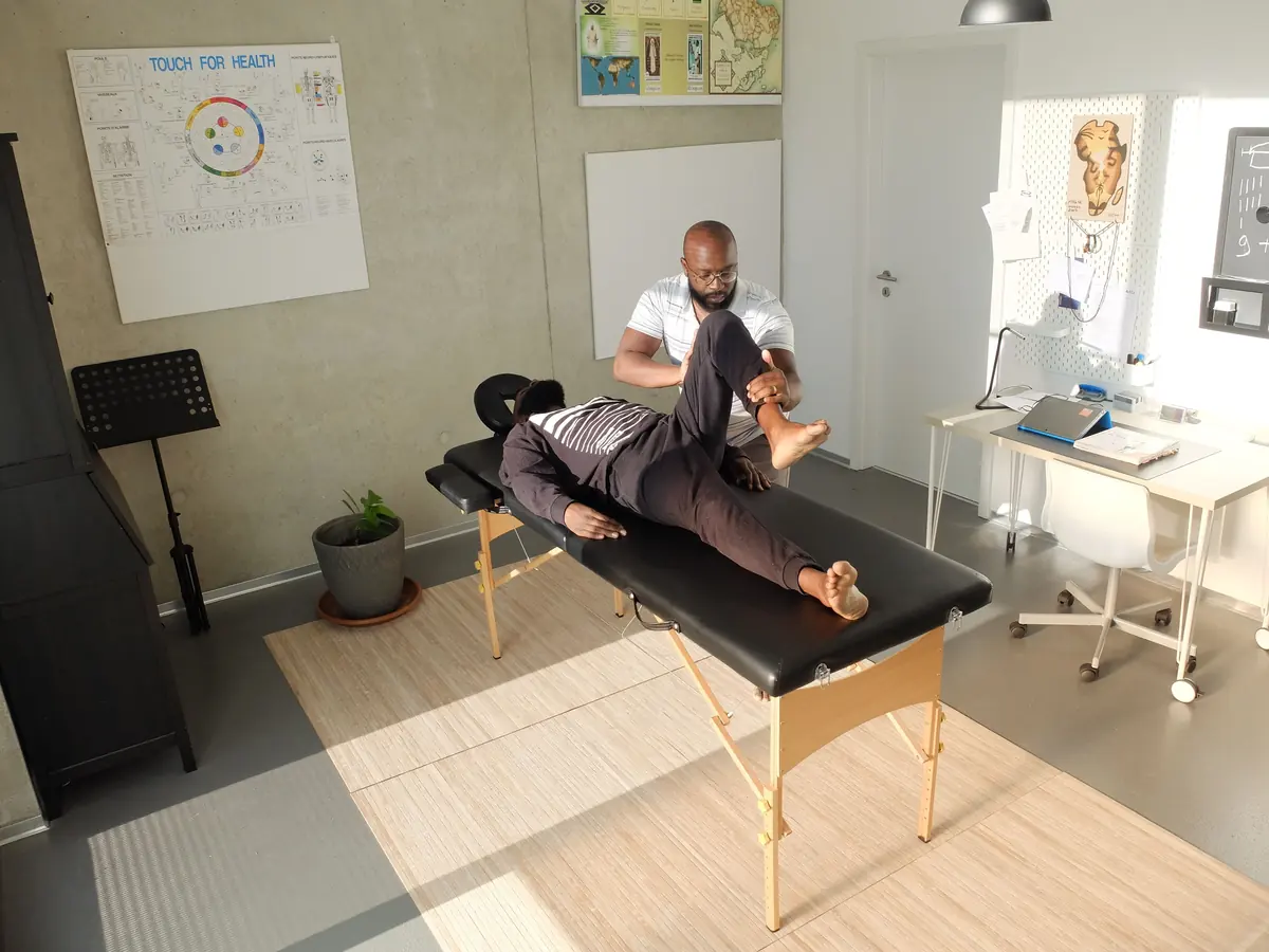 A therapist working with a client lying on a treatment table in a plain, bright room