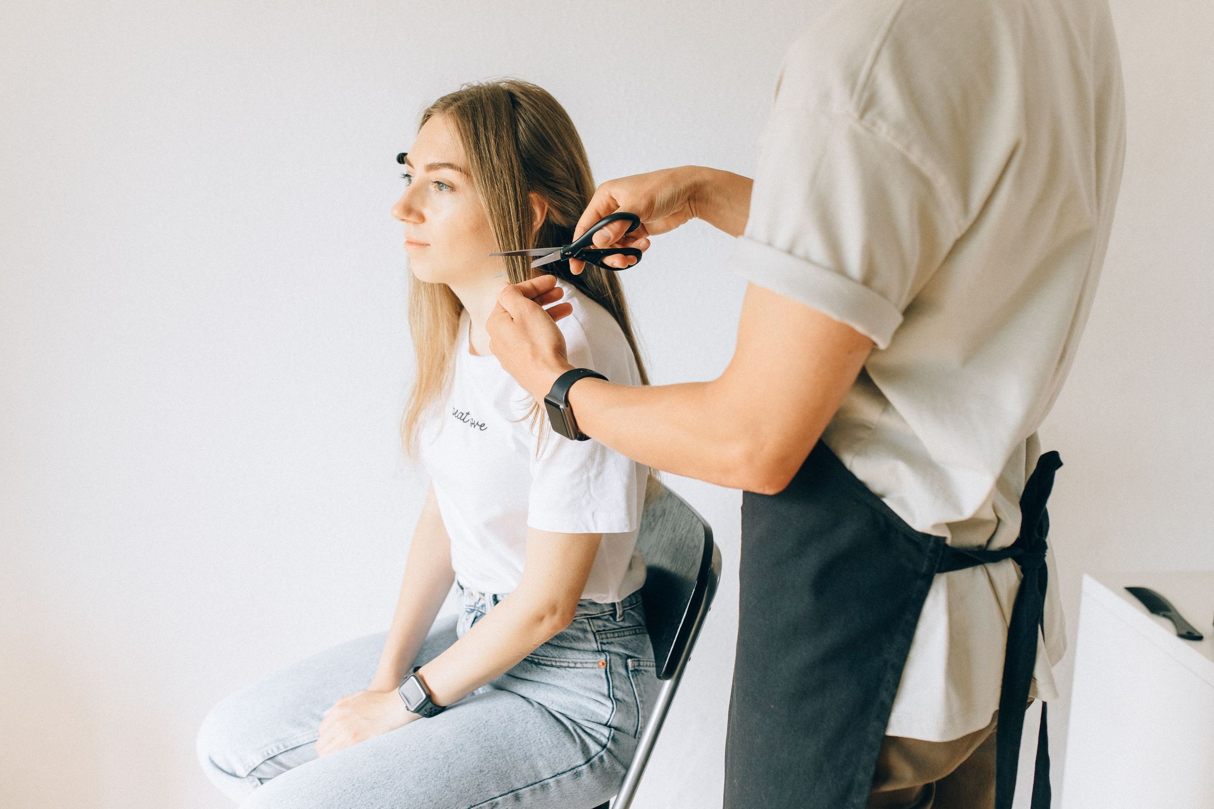 A stylist trimming a client&rsquo;s hair with scissors in a bright, modern salon