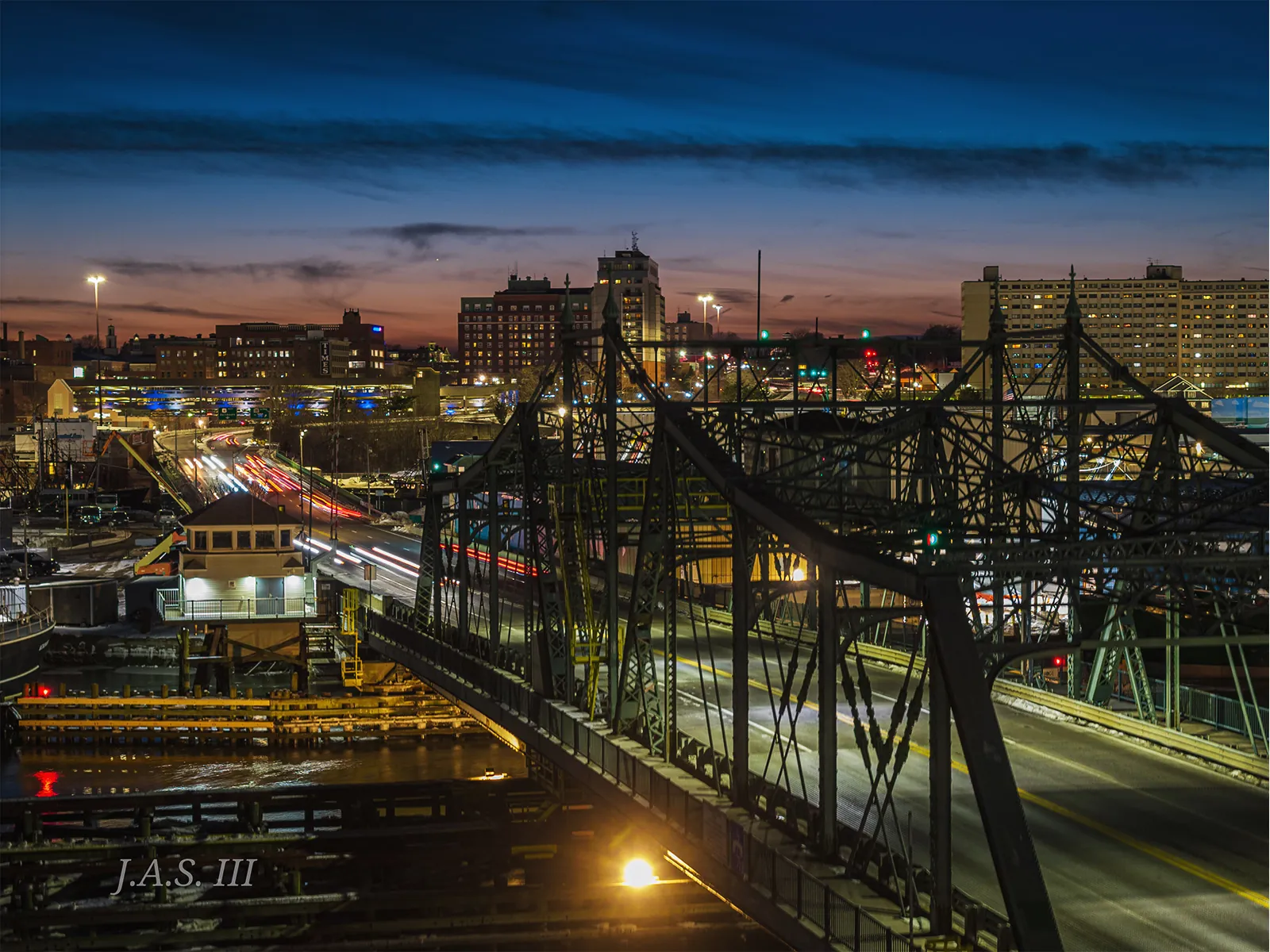 The swing bridge between New Bedford and Fairhaven after dark, with headlight trails on the road into the city