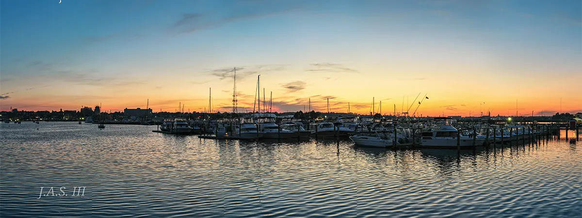 A marina at dusk with rows of moored boats and a calm harbor under an orange sky